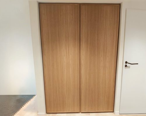 Fachada de armário em carvalho com portas altas e puxadores de topo invisíveis.