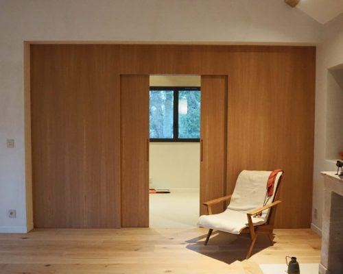 Portas de correr abertas em painel de carvalho permitindo a passagem entre a sala de estar e a sala de TV